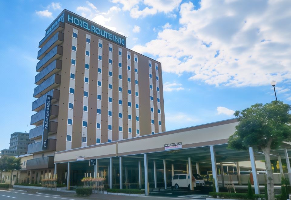 a large building with a hotel sign on the side and a car parked in front of it at Hotel Route-Inn Fuji Chuo Koen Higashi