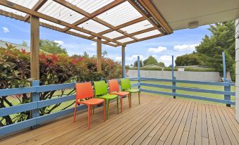 a wooden deck with a dining table and chairs , surrounded by lush greenery and a blue sky at North South Holiday Park