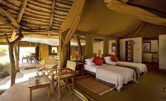 a bedroom with two beds , a chair , and wooden furniture under a thatched roof , creating a cozy and inviting atmosphere at Elewana Lewa Safari Camp