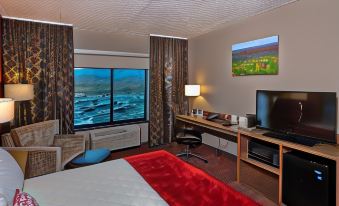 a modern hotel room with a large window offering a view of the ocean , red bedspread , desk , and other amenities at Shoshone Rose Casino & Hotel