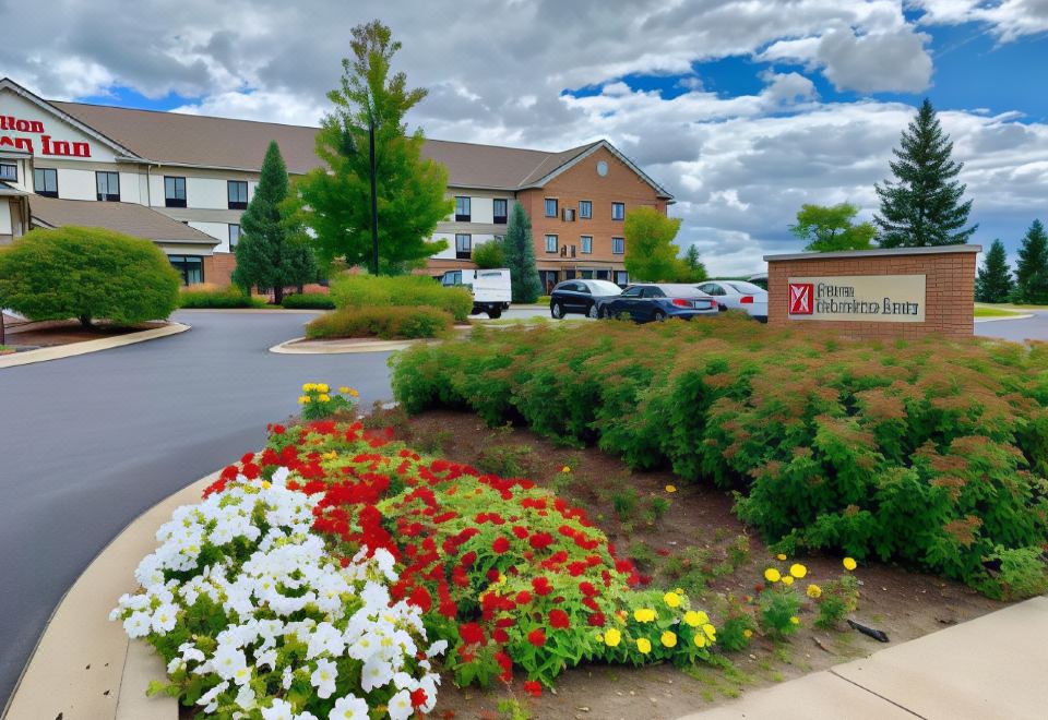 a hotel with a flower bed in front of it , surrounded by bushes and trees at Hilton Garden Inn Oconomowoc