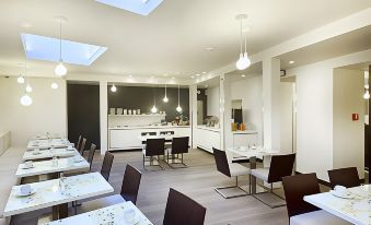 a modern dining room with white chairs and tables , a kitchen in the background , and pendant lights hanging from the ceiling at Pure White