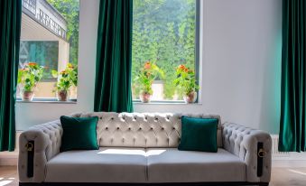 a white couch with green pillows is placed in front of a window with green curtains and potted plants at Hotel THR Center