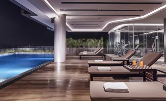 a modern swimming pool area with wooden floors , white umbrellas , and towels near the pool , while another lounge chair and a wall of windows offer at Front One Boutique Karawang