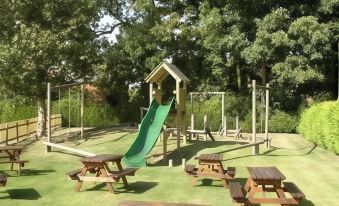 a wooden playground with swings , slides , and picnic tables is set up in a grassy area at Thornton Hunt Inn