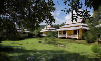 a serene scene of a lake with three yellow and white houses , surrounded by lush greenery at Poonyamantra Resort