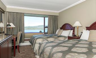 a hotel room with two beds , a window offering a view of the ocean , and lamps on both sides of the bed at Crest Hotel