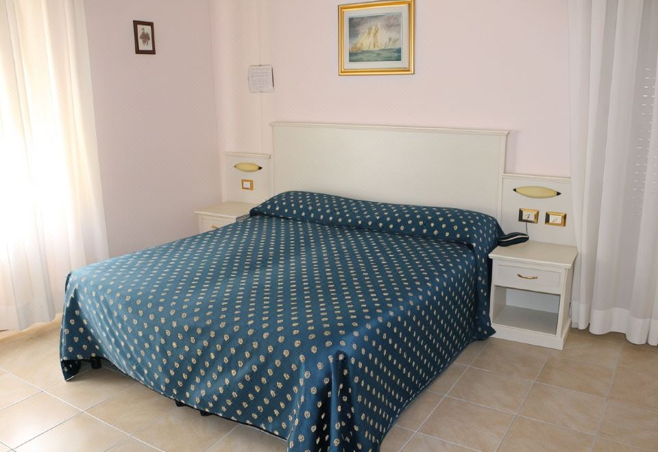 a neatly made bed with blue and gold patterned sheets , accompanied by white nightstands and a painting on the wall at Hotel Rio Sanremo