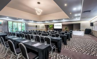 "a large conference room with rows of tables and chairs , a projector screen , and a sign reading "" salonura "" on the wall" at Waipuna Hotel & Conference Centre