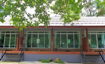 a modern house with large windows and wooden doors , surrounded by trees and a stone path at Baan Chao Mai Beach House