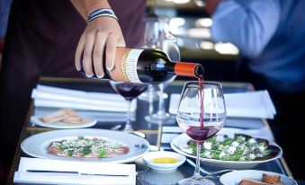 a man is pouring wine into a wine glass at a restaurant table , surrounded by various dishes at The Larwill Studio Melbourne - Art Series