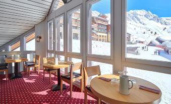 a dining area with several tables and chairs , overlooking a snowy mountain landscape through large windows at Hôtel l'Eden des Cimes - Vacances Bleues - Belle Plagne 2100