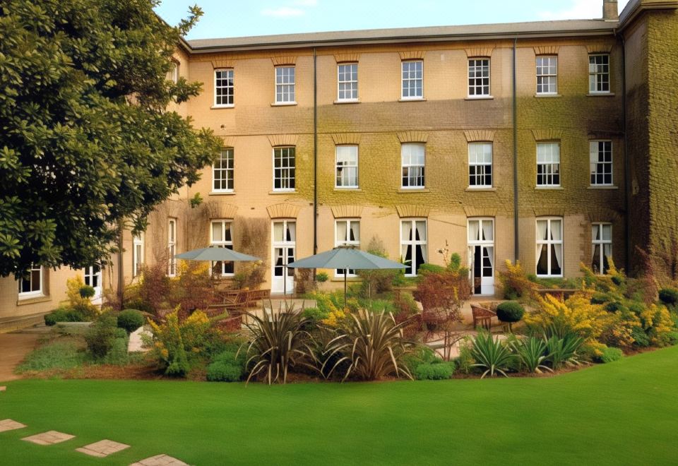 a large building with multiple windows and doors , surrounded by lush green grass and trees at De Vere Beaumont Estate