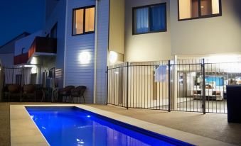 a modern , white house with a blue pool and fence in front of it , illuminated at night at Quest Bendigo Central