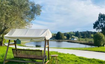 a wooden bench is situated on a grassy field near a body of water , with a tent in the background at De'Vine Escape