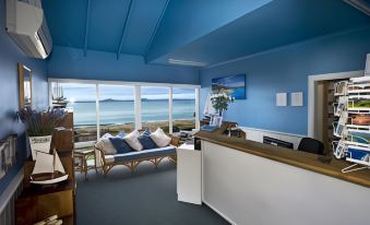 a room with a couch , chairs , and a desk is shown with a view of the ocean at Swansea Motor Inn Tasmania