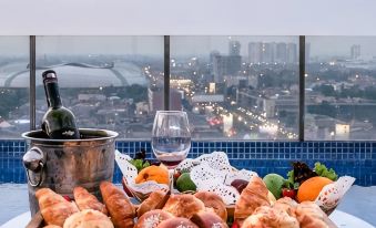 a wooden tray filled with various pastries and a glass of wine is placed on a table overlooking a city skyline at Aston Imperial Bekasi Hotel & Conference Center