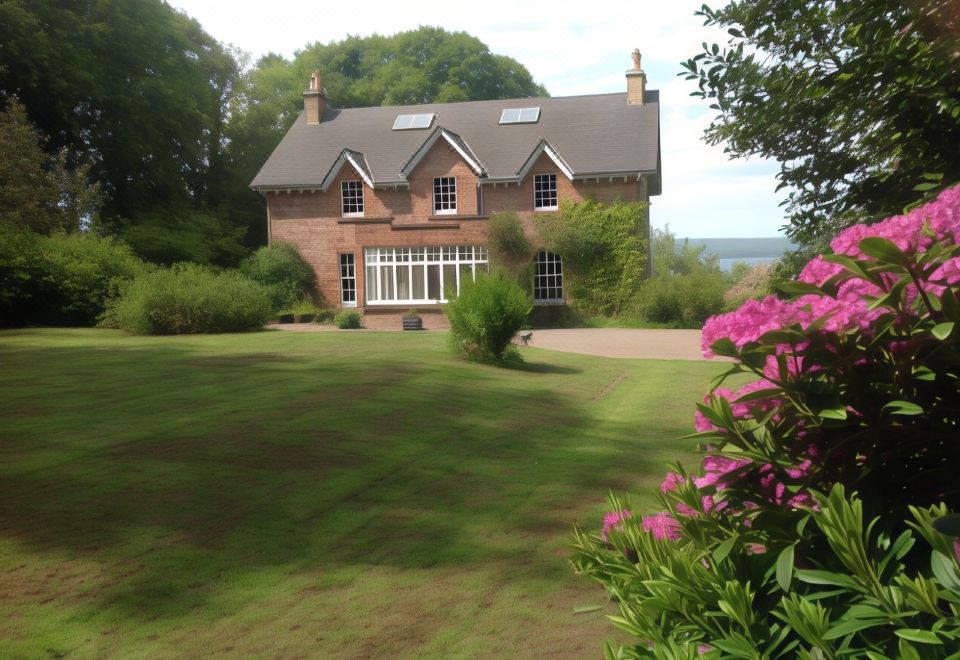 a large house with a brick exterior and windows is surrounded by greenery and pink flowers at The Factor's House