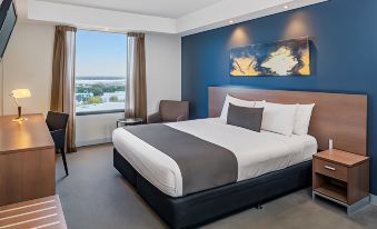 a large bed with white and gray linens is in a room with a view of the ocean at Mantra Melbourne Airport