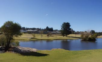 a serene golf course with a pond in the foreground , surrounded by green grass and trees at Girraween Environmental Lodge