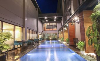 an indoor swimming pool surrounded by a building , with several people enjoying their time in the pool at Swiss-Belinn Timika