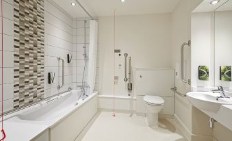 a modern bathroom with white walls , a toilet , a bathtub , and a shower area with rails at Premier Inn Merthyr Tydfil