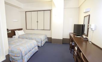 a hotel room with two beds , a desk , and a tv , all neatly arranged on a blue carpet at Toyota Village