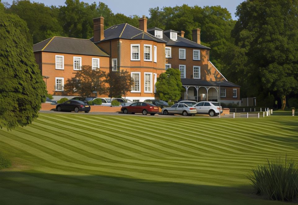 a large , red brick building with multiple windows , surrounded by lush green grass and trees , with cars parked in front of it at Brandshatch Place & Spa