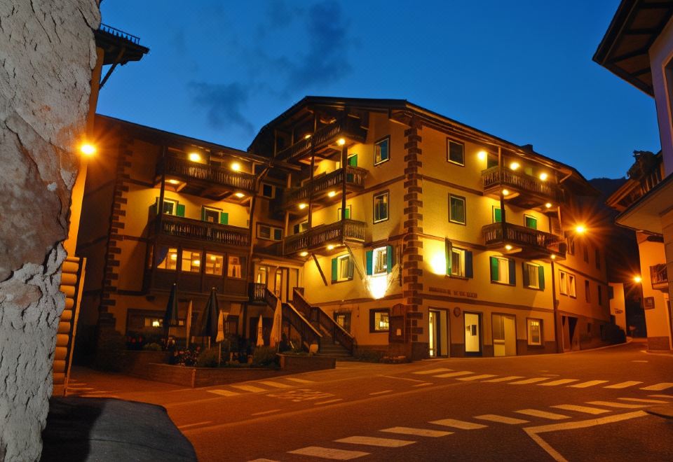 a building with green windows and a blue sky in the background , lit up at night at Hotel Alpino