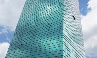 a tall , modern building with a blue glass facade is situated under a cloudy sky at Bay Hotel Srinakarin