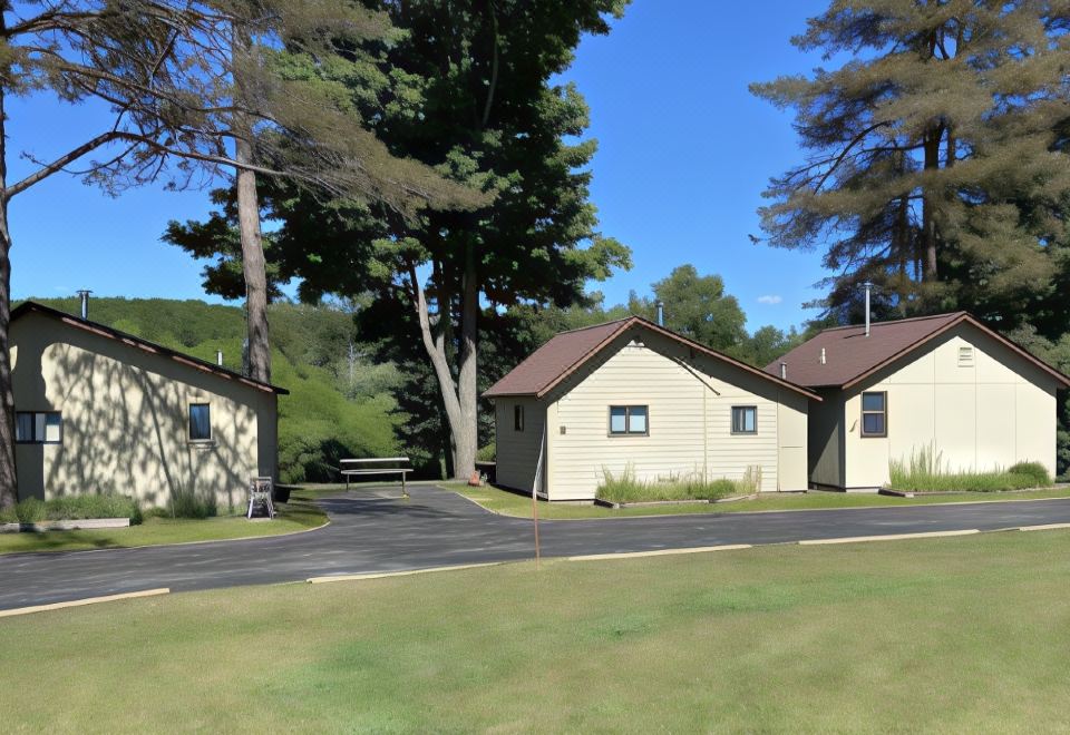 a driveway leading up to a house with a large tree in the background , surrounded by grass and trees at Betsie Riverside Resort