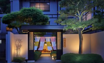 a japanese - style house with a colorful gate and lanterns , surrounded by trees and lit up at night at Moritaya