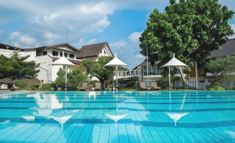 a large outdoor swimming pool surrounded by a hotel , with several umbrellas and lounge chairs placed around the pool area at Front One Resort Magelang