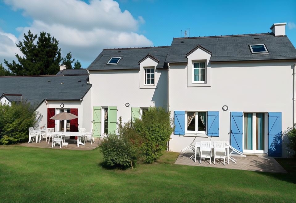 a white house with blue shutters and a green lawn in front of it , surrounded by trees at Lagrange Vacances le Hameau de Peemor PEN
