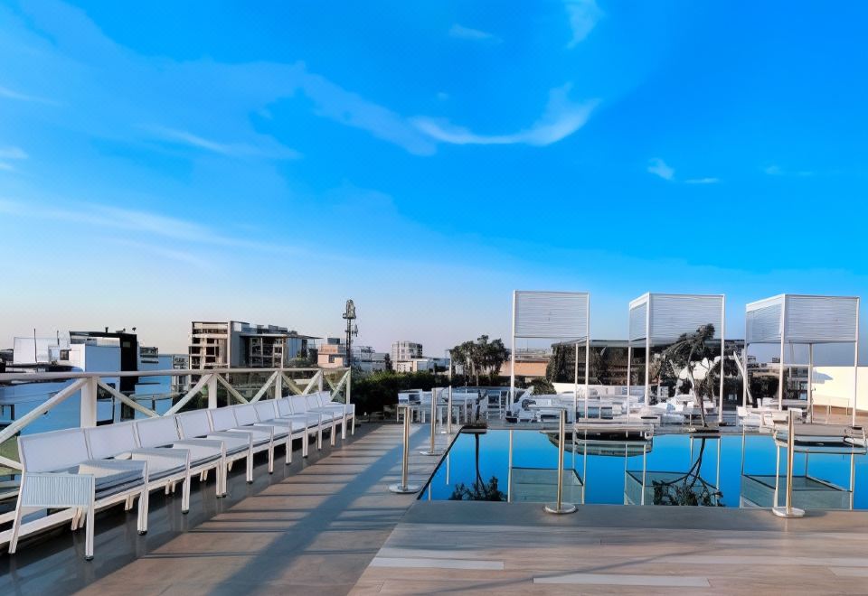 a large outdoor swimming pool surrounded by white lounge chairs and umbrellas , with a city skyline in the background at Hotel Centre Point