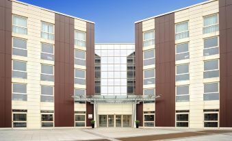 a modern building with large windows and a glass canopy entrance , surrounded by a clear blue sky at Idea Hotel Milano Malpensa Airport