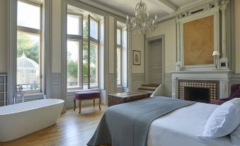 a large bedroom with a bed , bathtub , and fireplace , as well as a chandelier hanging above the bed at Chateau les Carrasses