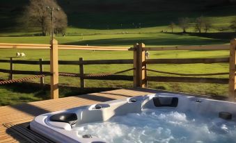 a hot tub on a wooden deck , surrounded by green grass and a beautiful view of a golf course at The Hand at Llanarmon