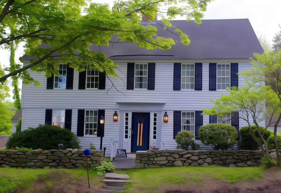 a white house with black shutters and blue doors , surrounded by trees and a stone wall at Spring Hill Inn