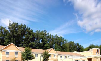 a large , yellow and white building with trees in the background , under a clear blue sky at Comfort Inn & Suites Saratoga Springs