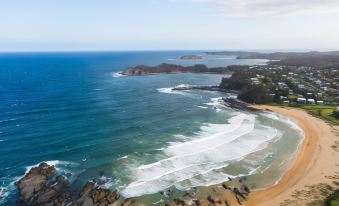 an aerial view of a sandy beach near the ocean , with waves crashing against the shore at Abode Malua Bay