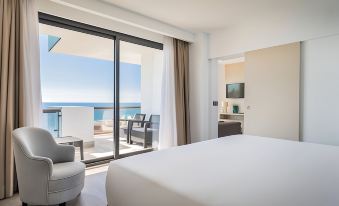 a modern hotel room with large windows offering an ocean view , white bedding on the bed , and a comfortable seating area at Occidental Fuengirola