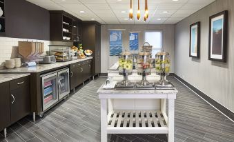 a hotel breakfast bar with various food items and beverages , including bowls of fruit and a white table with metal racks at Homewood Suites by Hilton Chicago-Lincolnshire