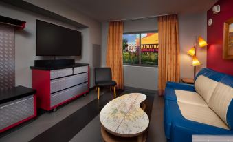 a modern living room with a large window , blue couch , red ottoman , and a television at Disney's Art of Animation Resort