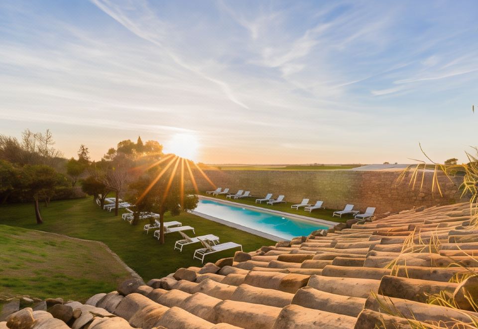 a large outdoor pool surrounded by lounge chairs and a hot tub , with the sun setting in the background at Baglio Occhipinti