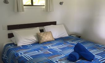 a bedroom with a blue and white quilt on a bed , a window with curtains , and a rug on the floor at Alstonville Country Cottages