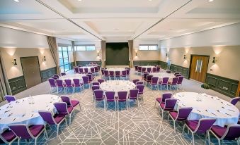 a large , empty conference room with purple chairs and white tables is set up for a formal event at Denham Grove