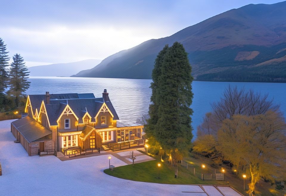 a large house with a red roof is situated next to a body of water at The Whispering Pine Lodge