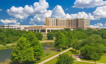 a large hotel surrounded by green grass and trees , with a pond in the background at Sheraton Austin Georgetown Hotel & Conference Center