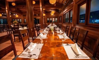 a long dining table is set with white napkins and wine glasses in a large room with wooden walls at Tam Coc La Montagne Resort & Spa